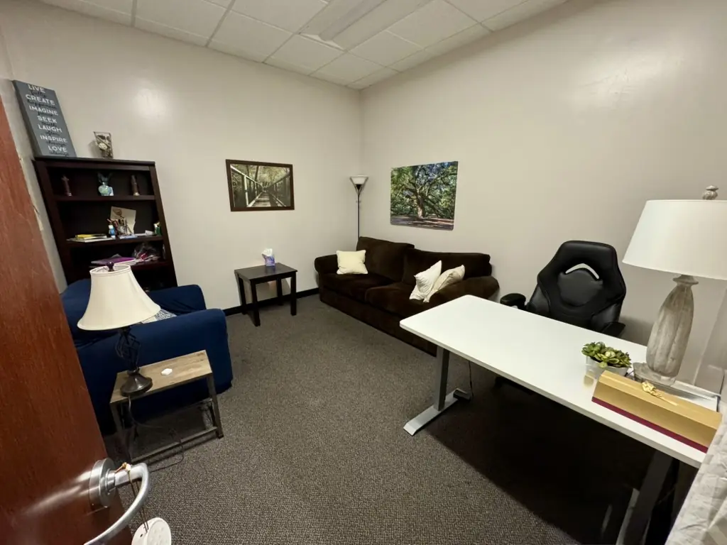 A furnished office with a brown leather sofa and a desk