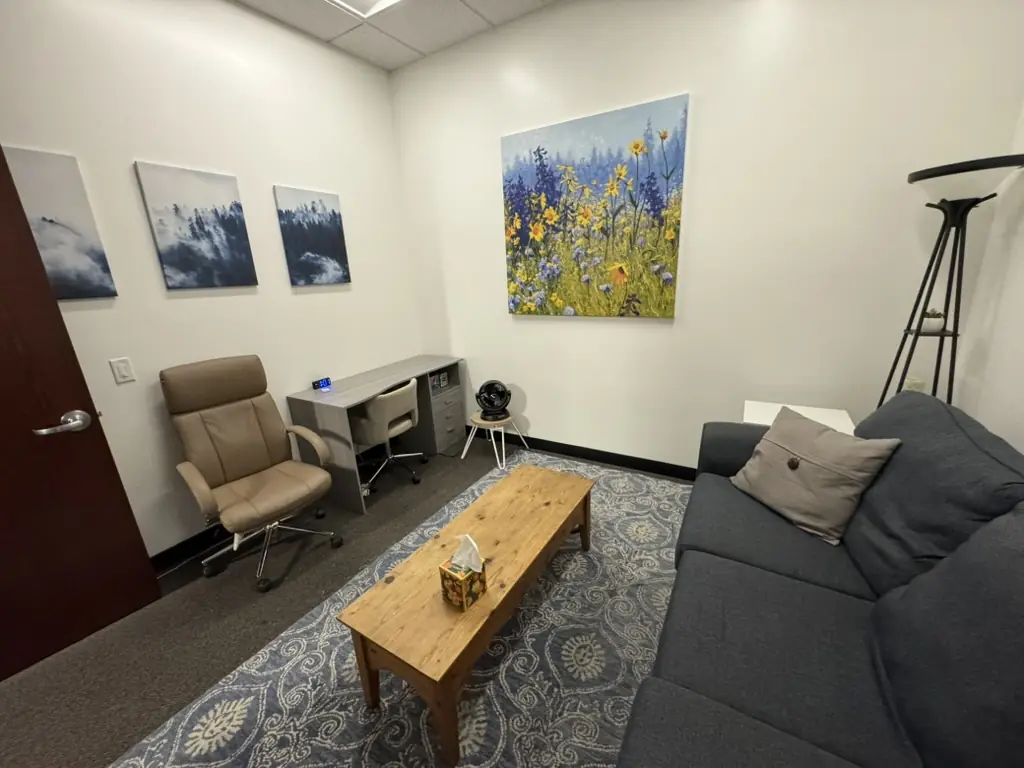 A furnished office with a blue rug, a sofa, and an armchair