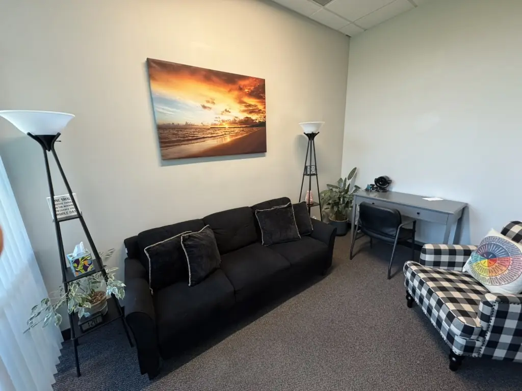A furnished office with a large window, a sofa, and an armchair