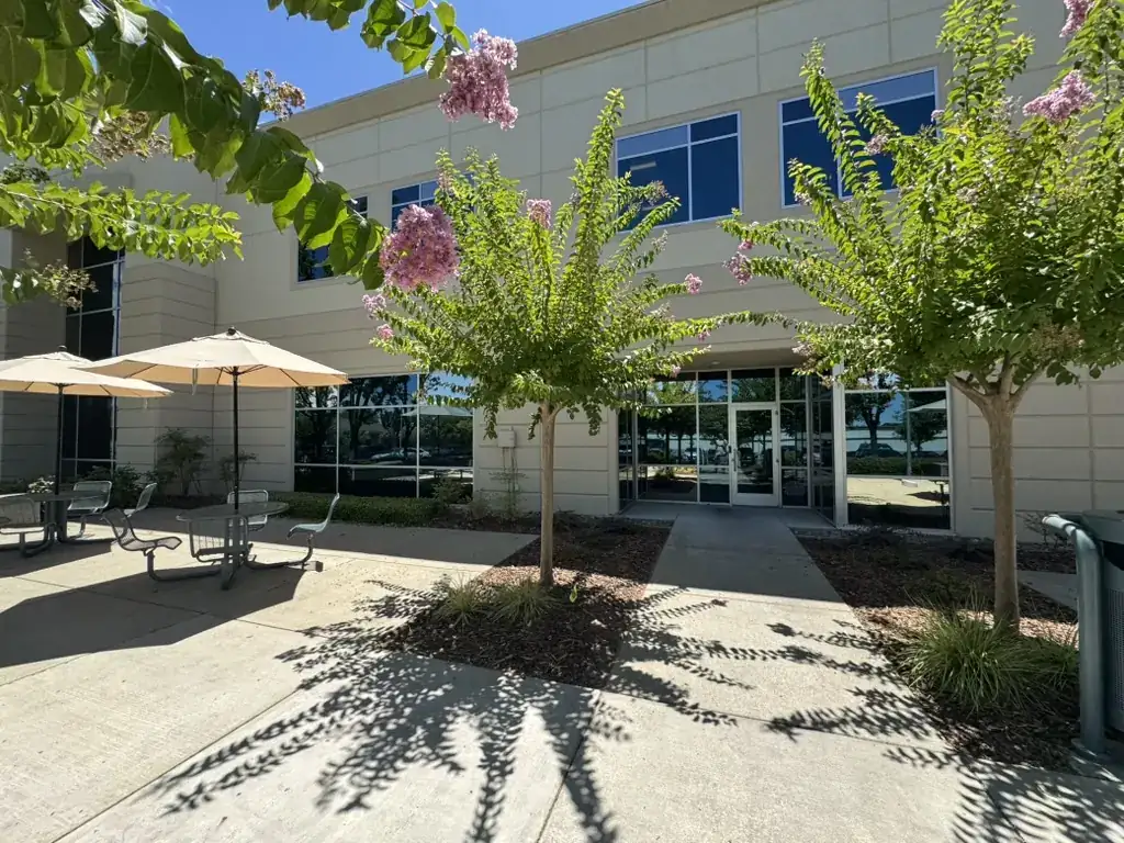 The back entrance of the Blue Oaks office building with a shaded patio and green lawn in summer